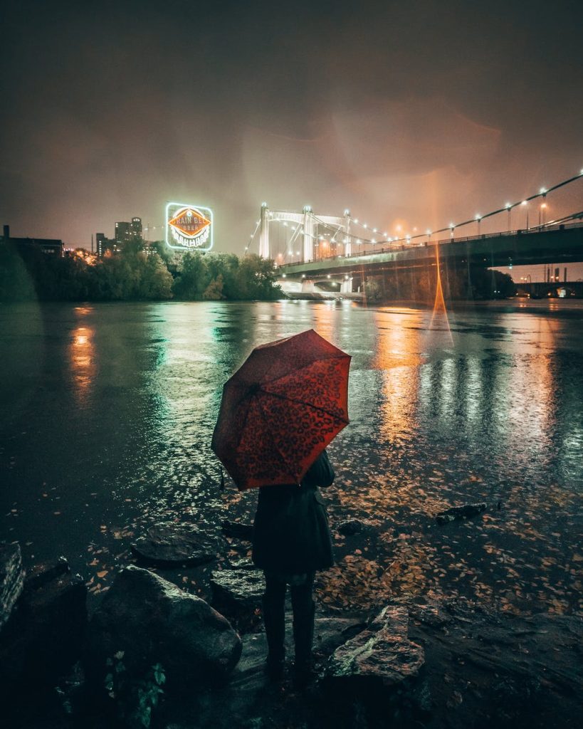 woman with red umbrella standing at riverbank