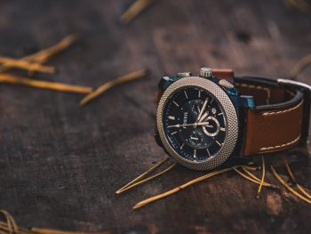 round silver colored fossil chronograph watch with brown leather band on brown wooden surface