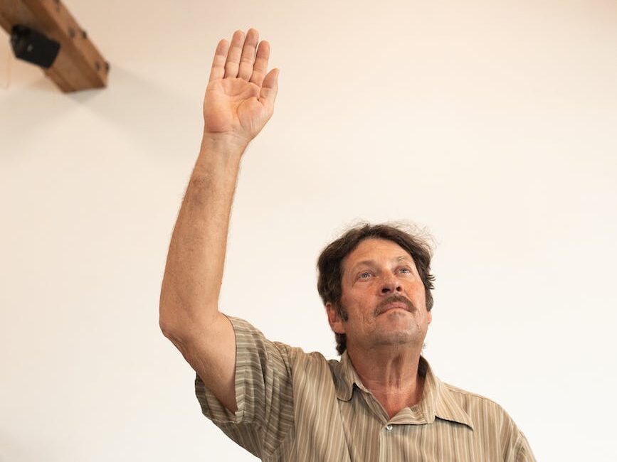 adult man in brown and white striped button up shirt raising his hand