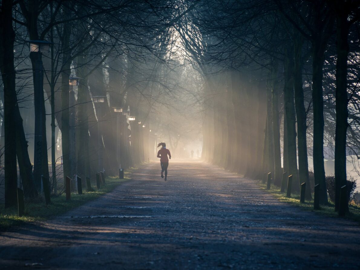 person running near street between tall trees